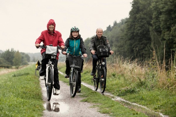 Portrait of grandparents and granddaughter cycling on wet field against clear sky