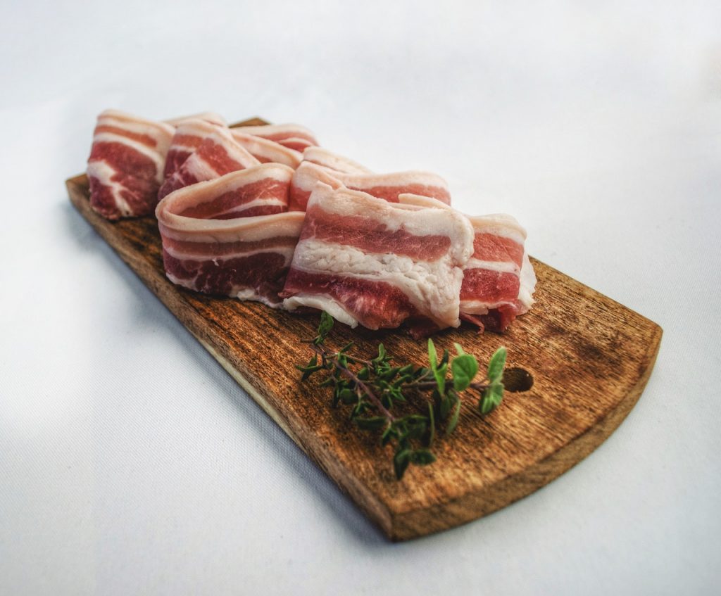 Slices of thick raw bacon on cutting board.