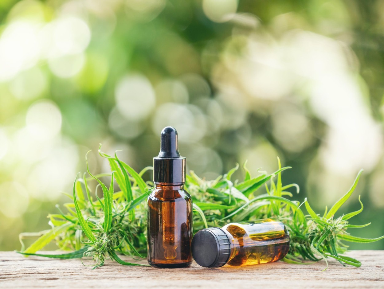 Two small bottles of CBD oil on a table with greenery in the background